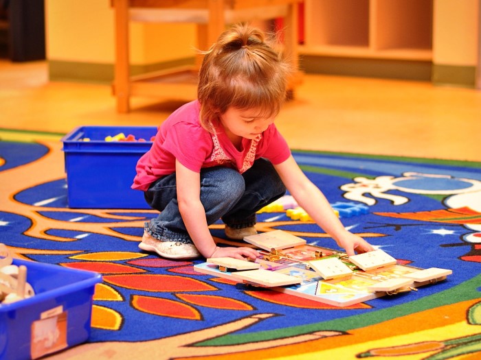 A little girl is looking at books whuch are laying on the carpet in EarlyON Years Centre