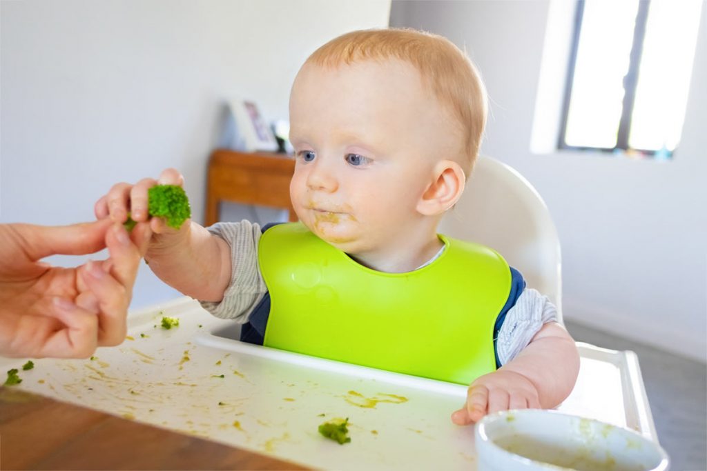 Baby taking broccoli from mom